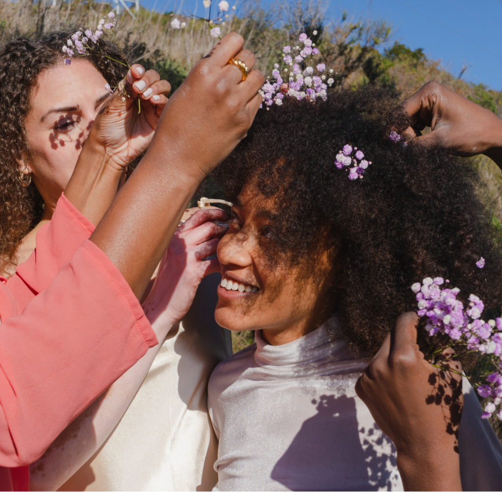 Two women with curly hair outdoors, surrounded by flowers, with a promotional message about caring for curls.